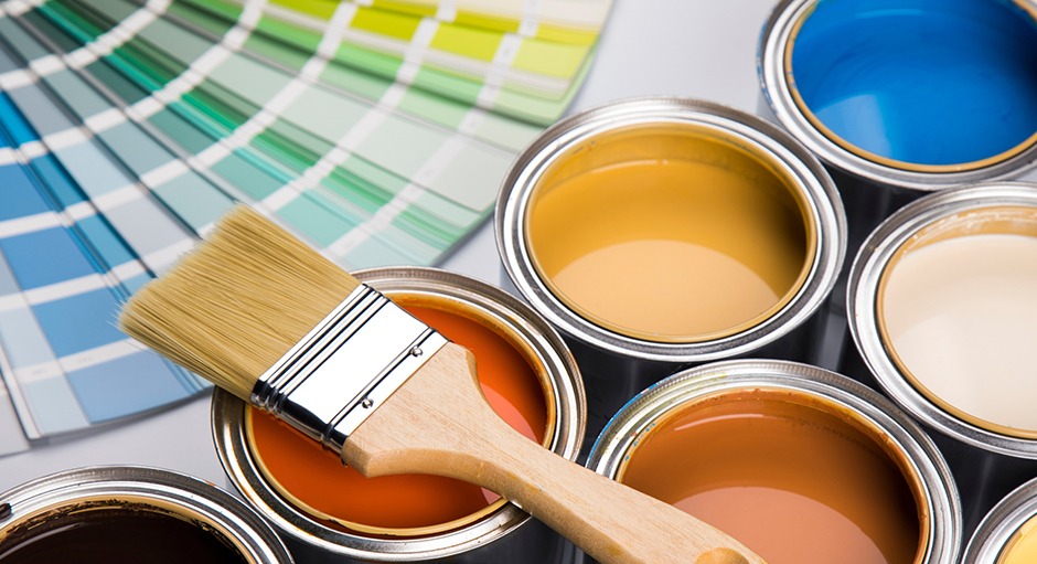 Mehrere kleine Farbeimer, auf denen ein Pinsel liegt. Im Hintergrund sind Farbfächer von Sonderfarben zu sehen.