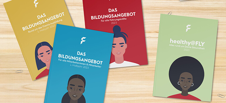 Vier farbige Broschüren zu den Bildungs- und Gesundheitsangeboten für Mitarbeitende liegen auf einem Holztisch.