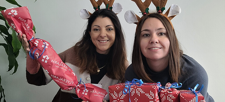 Zwei Frauen mit Rentier-Accessoires halten einen Adventskalender in Bonbonform in die Kamera.