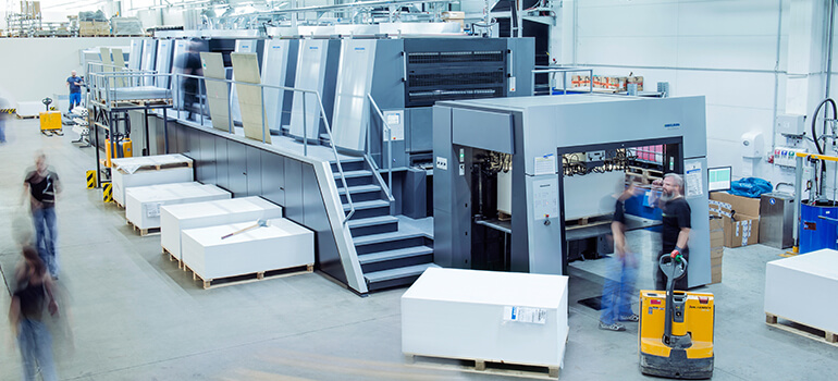 Große Druckmaschine in einer modernen Produktionshalle von Flyeralarm, Menschen arbeiten im Hintergrund.