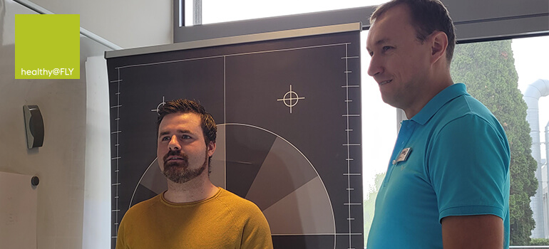 Zwei Männer bei einer Haltungsanalyse vor einer Messwand mit Zielmarkierungen.