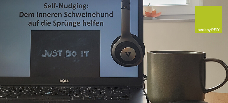 Laptop mit der Aufschrift „Self-Nudging: Dem inneren Schweinehund auf die Sprünge helfen“, daneben Kopfhörer und Kaffeetasse.
