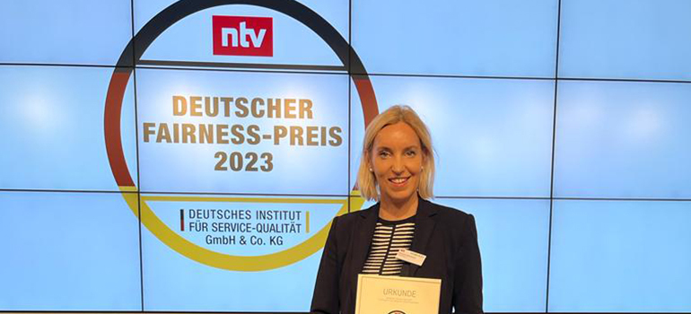 Frau hält Urkunde vor Wand mit Logo Deutscher Fairness-Preis 2023 vom Deutschen Institut für Service-Qualität.
